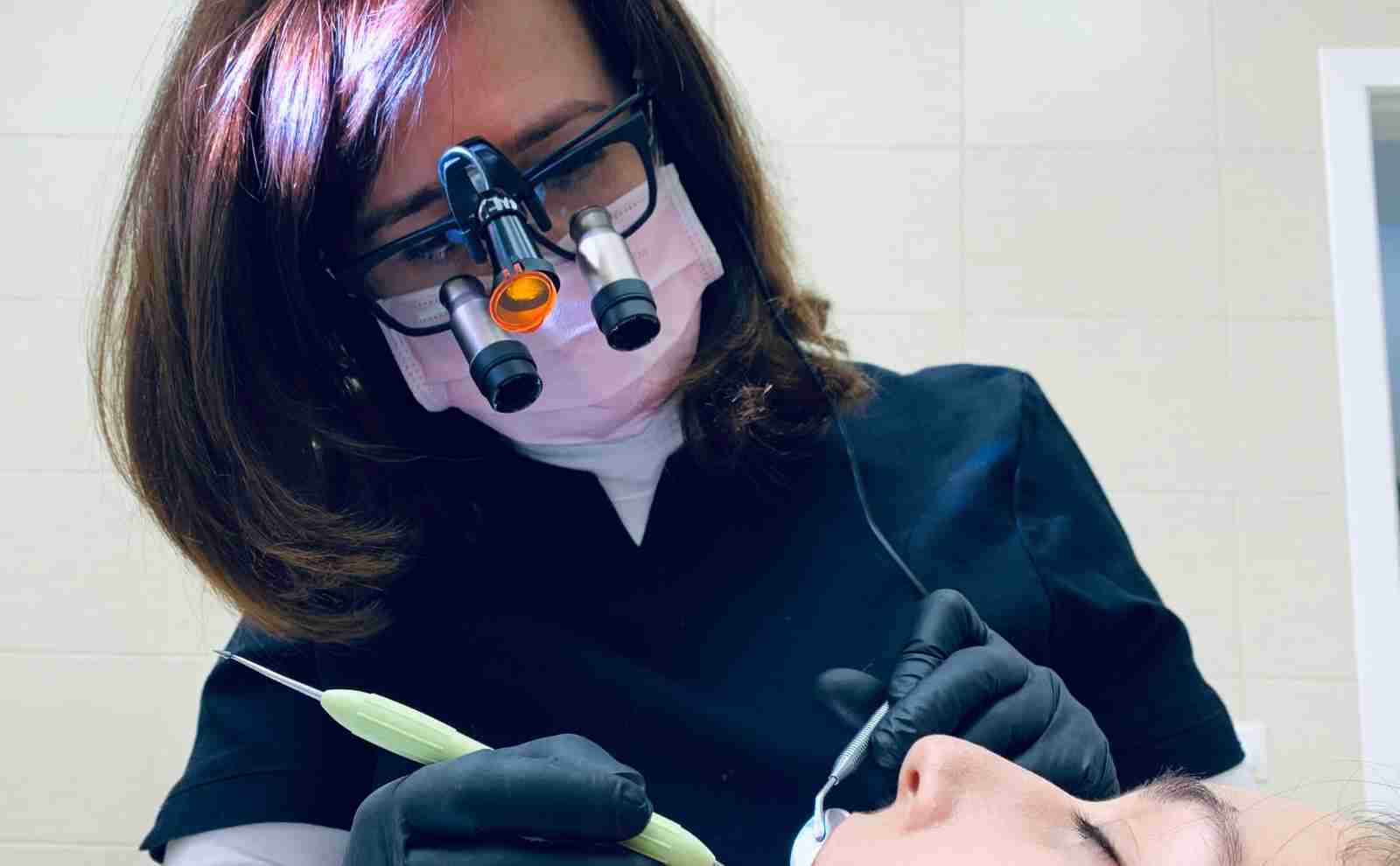A woman dentist wearing loops, a mask and gloves while working with a patient